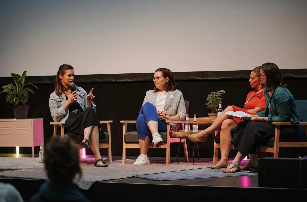 Four participants in a panel discussion; the speaker on the left is holding a microphone.